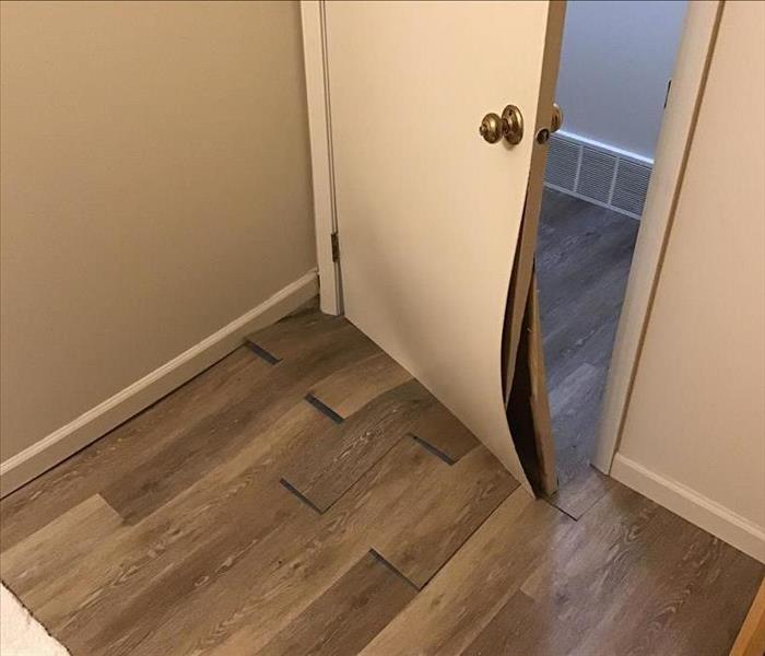 Majorly bowed flooring from water damage and door bowed from having to break it to get into room
