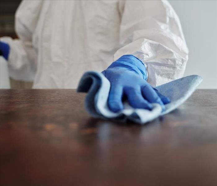 Person cleaning surface with blue rags in PPE