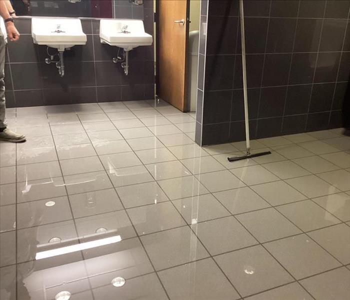 Inch of standing water in restroom, reflecting ceiling lights
